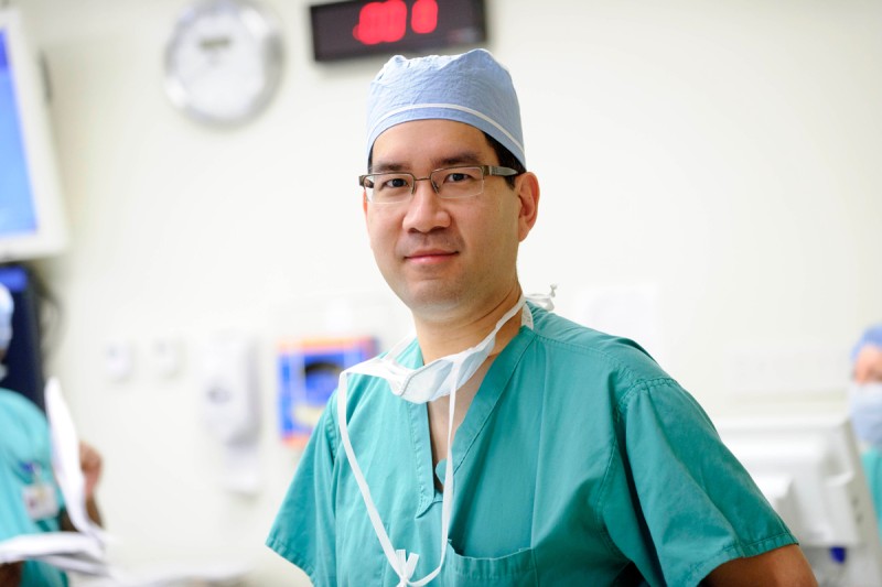 Doctor in green surgical scrubs wearing glasses and cap looking at camera.